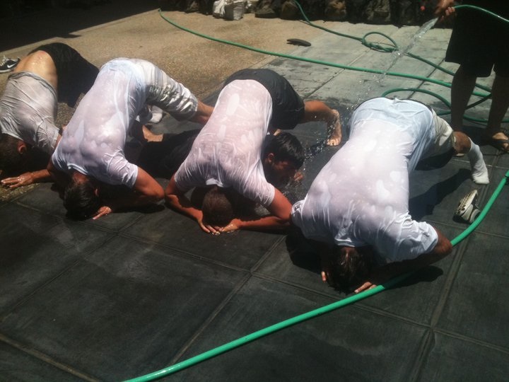 Men in wet shirts doing push-ups outdoors.