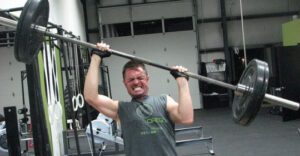 Man lifting heavy barbell in gym, showing effort and strength.