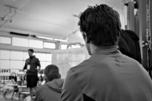 Men in gym focusing on instructor, black and white.