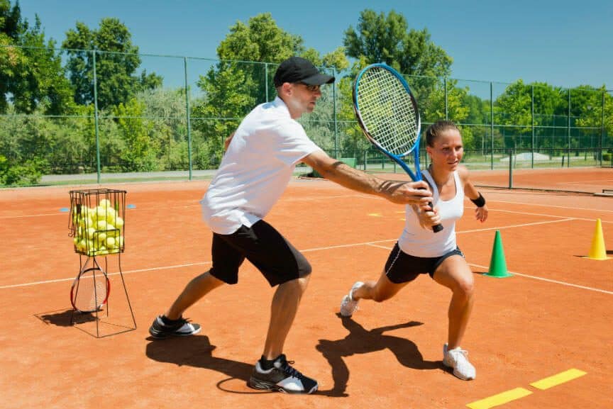 Tennis coach giving lesson to female player on clay court.