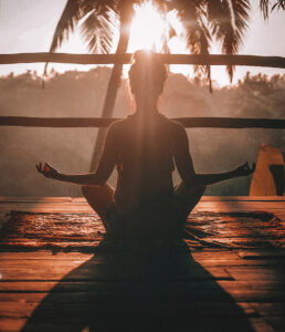 Woman meditating at sunset, tropical setting.