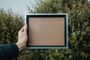 Hand holding blank corkboard frame outdoors.