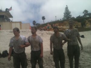 Four men covered in mud at the beach.