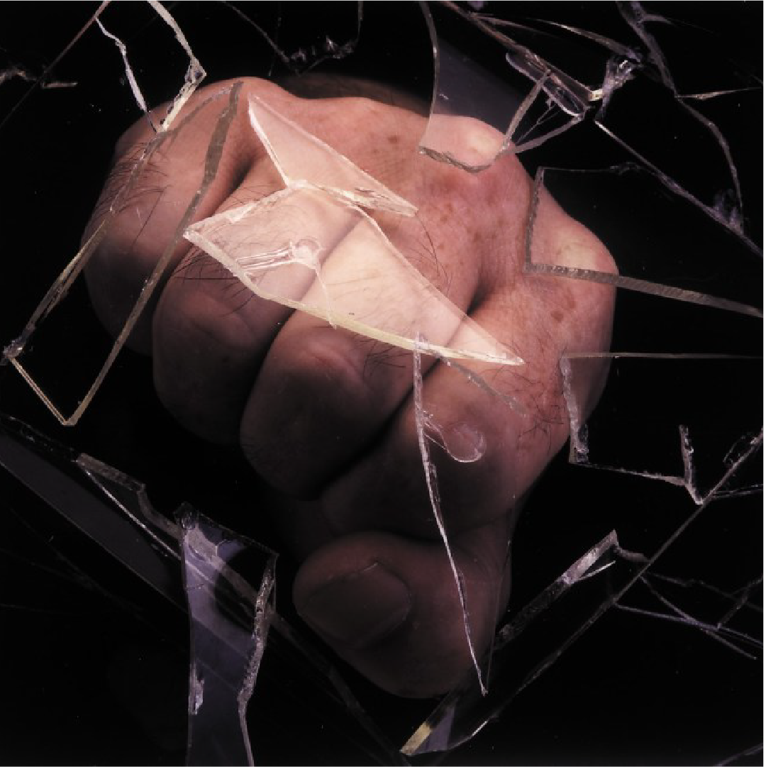 Hand punching through shattered glass, close-up view.