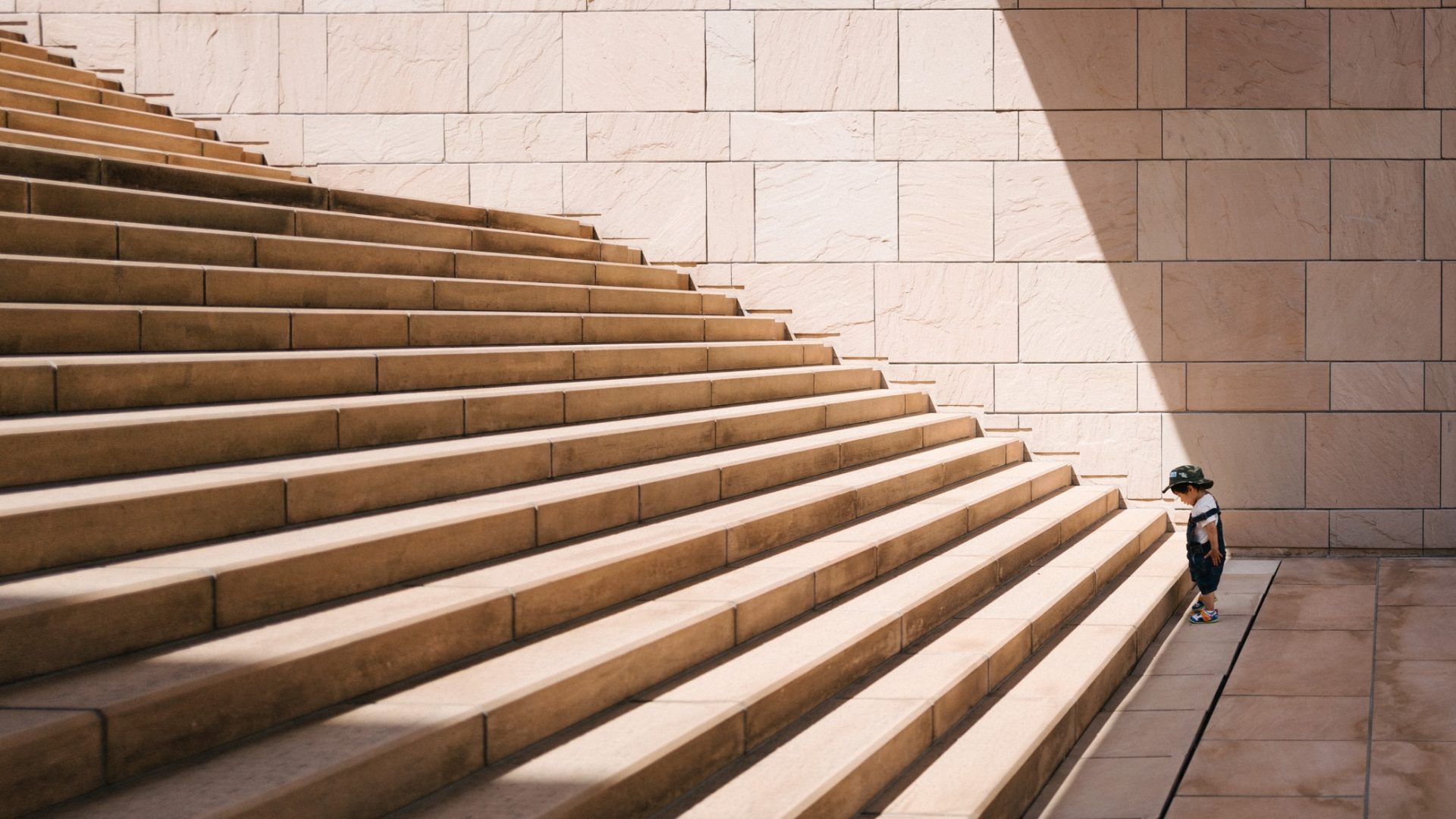 Child walking up large stone staircase, sunny day.