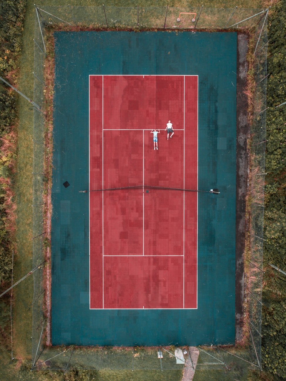 Aerial view of people playing tennis on red court.