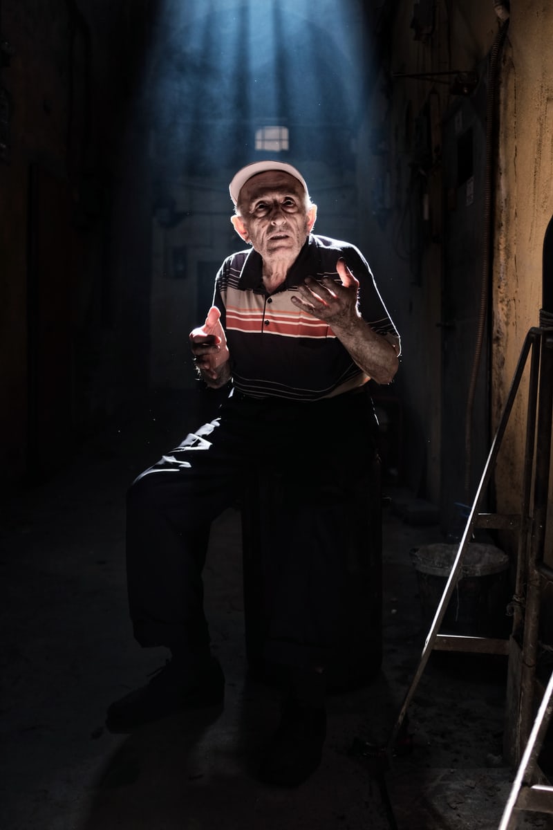 Elderly man talking in sunlit alleyway.