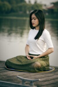 Woman meditating by lake in serene setting.