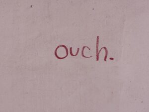 Red 'ouch.' text graffitied on a pale wall.