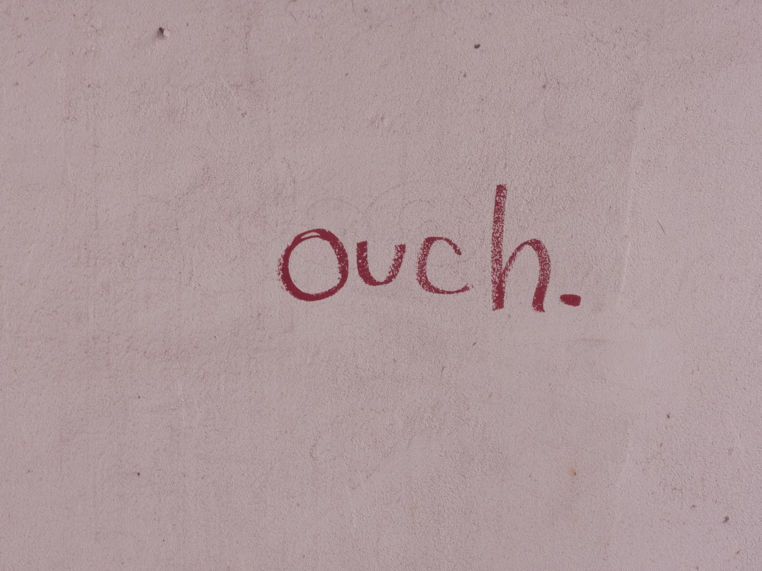 Red 'ouch.' text graffitied on a pale wall.