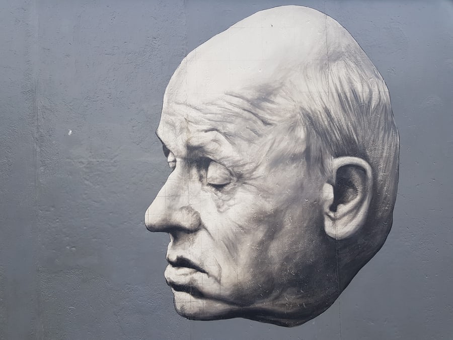 Monochrome sculpture of an elderly man's face on wall.