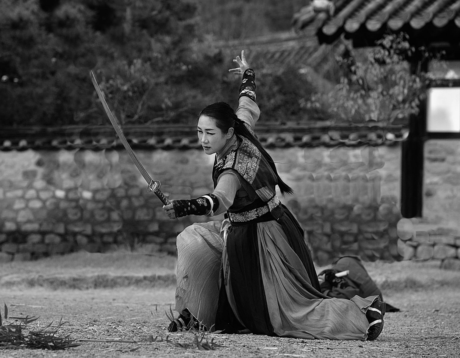 Woman practicing swordsmanship in traditional attire, monochrome.