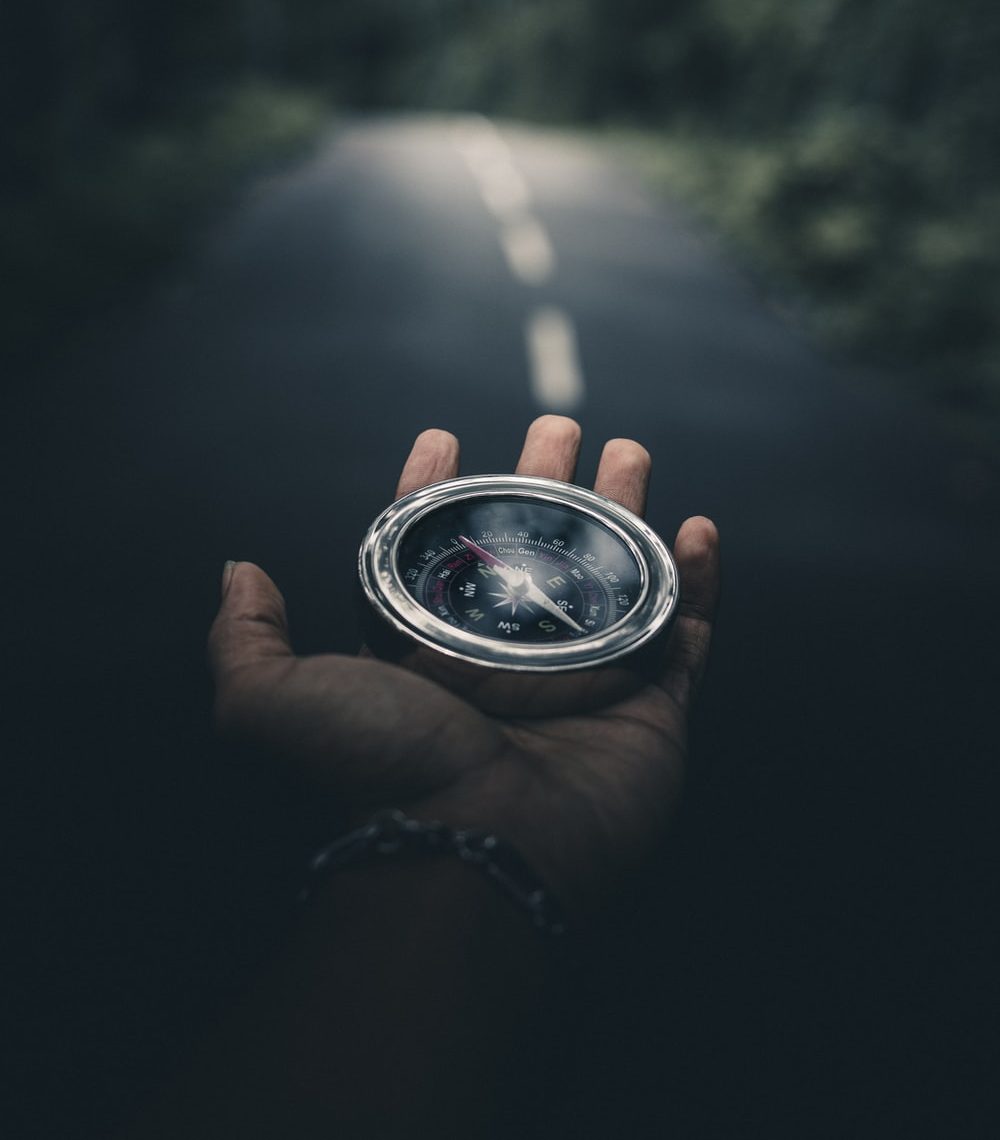 Hand holding compass on forest road.