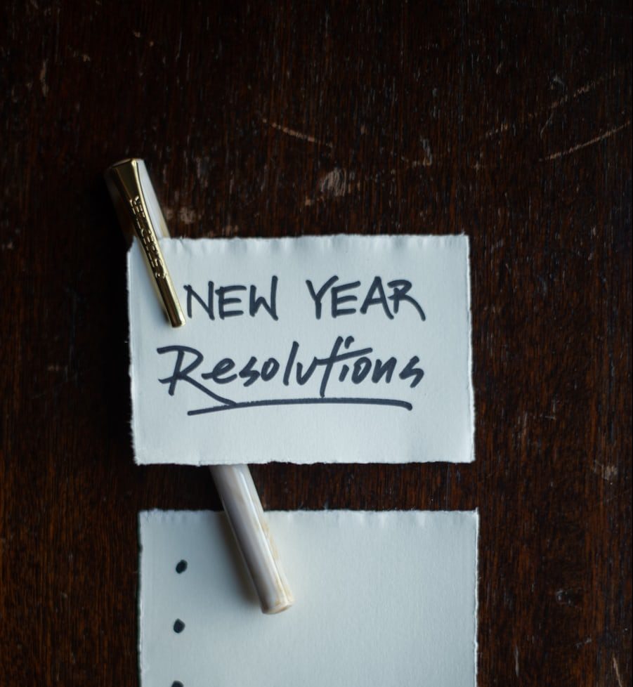 New Year resolutions list with pen on wooden table.