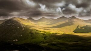 Dramatic stormy skies over lush, rolling green mountains.