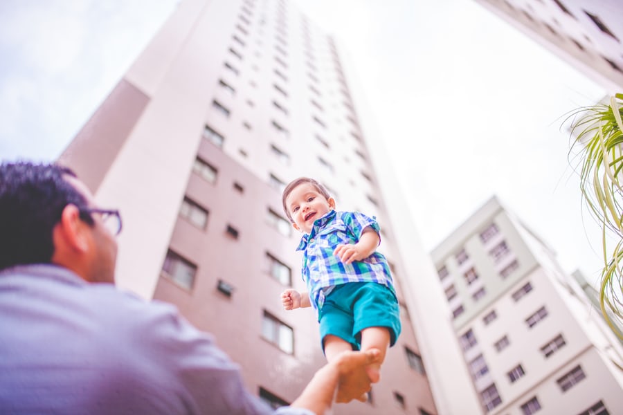 Father playing with toddler near high-rise buildings.