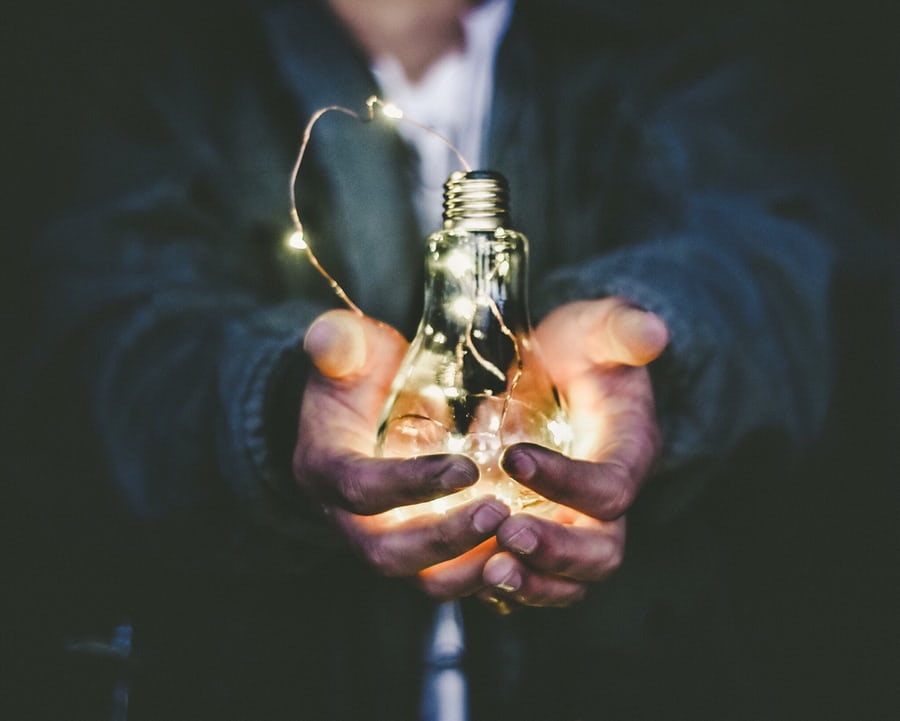 Person holding illuminated light bulb in dark setting.