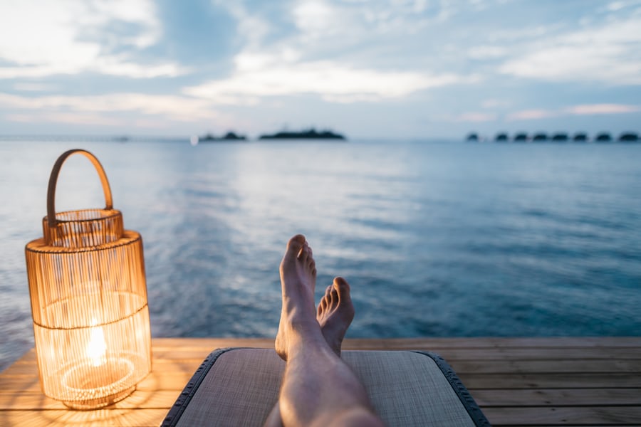 Relaxing oceanfront view with feet and lantern at sunset.