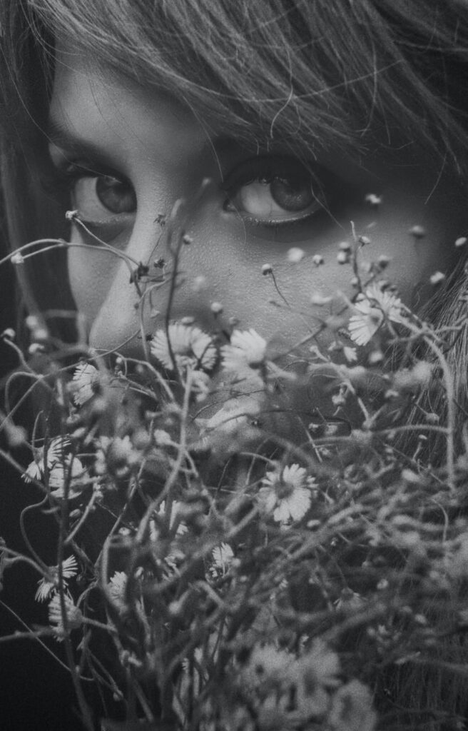 Woman's eye peeking through wildflowers, black and white portrait.