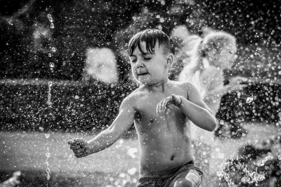 Boy playing joyfully in water sprinkles, black and white.