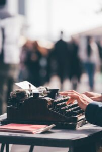 Person typing on vintage typewriter at outdoor setting.