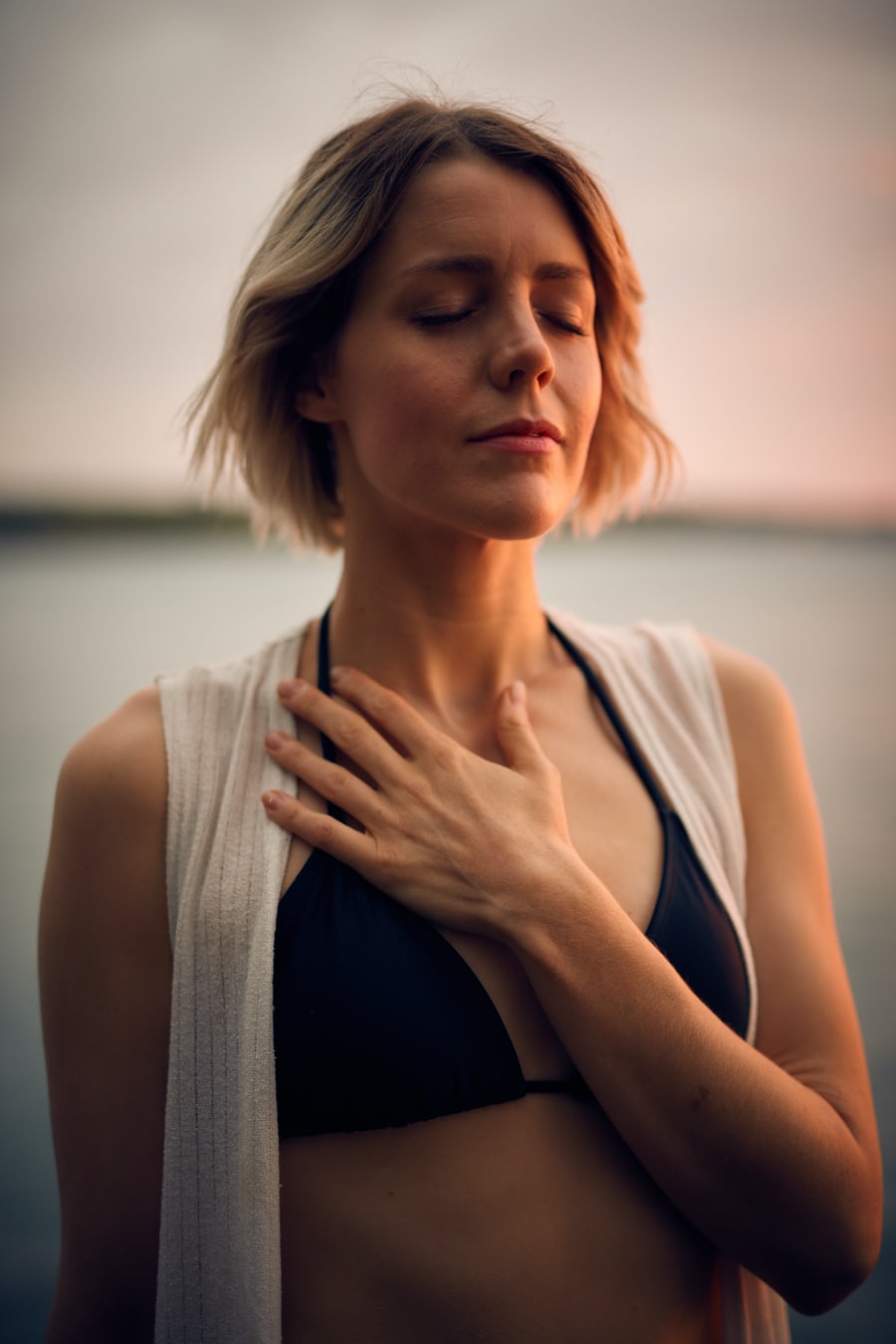 Woman meditating peacefully by the water at sunset.