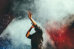 Singer raising hand in colorful concert smoke.