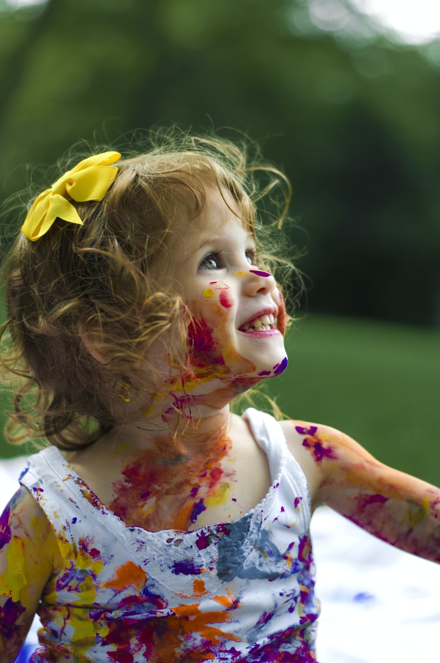 Joyful toddler covered in colorful paint outdoors.