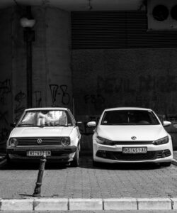 Two Volkswagen cars parked in graffiti-lined alley, monochrome.