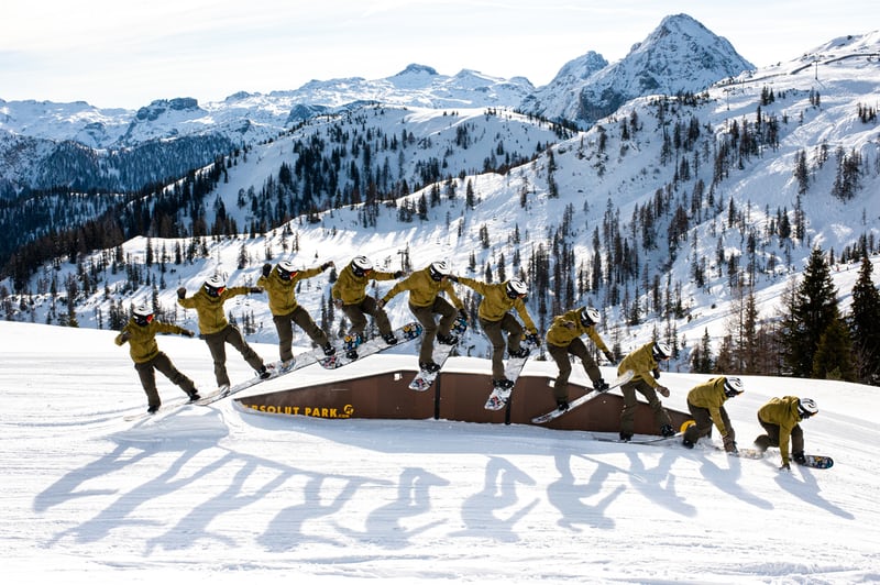 Snowboarder performing trick sequence in snowy mountain park.