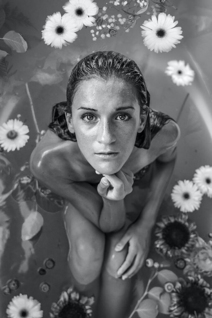 Woman surrounded by flowers in monochrome water bath.