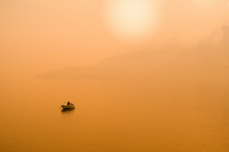 Boat on misty golden lake under hazy sun.