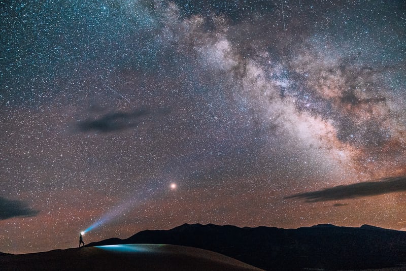 Person with flashlight under starry night sky.