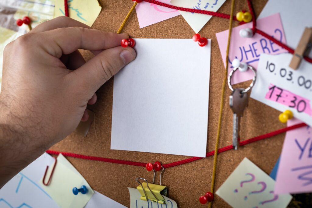 Hand pinning blank note on busy corkboard.