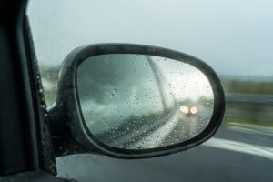 Rainy road viewed in car's side mirror.