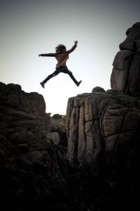 Person leaping between rocky cliffs at sunset.