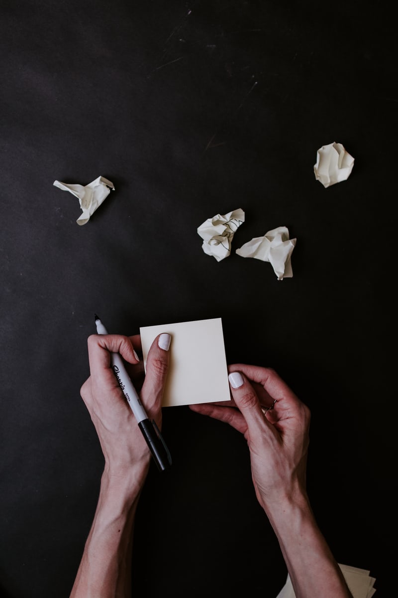 Person writing on note amid crumpled paper balls.