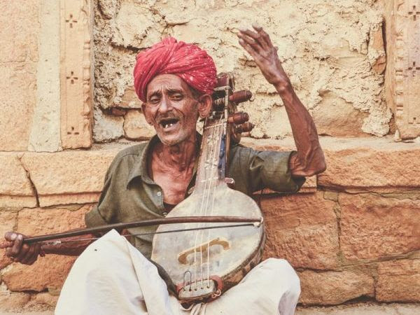 Elderly man playing traditional stringed instrument against wall.