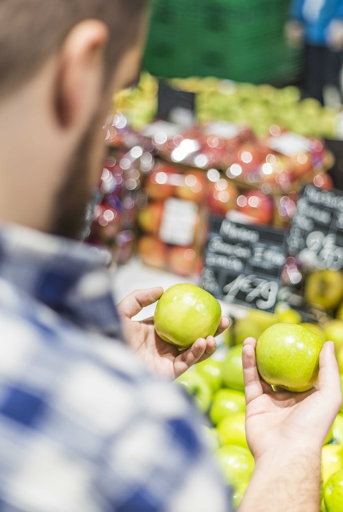 Man comparing apples in grocery store.