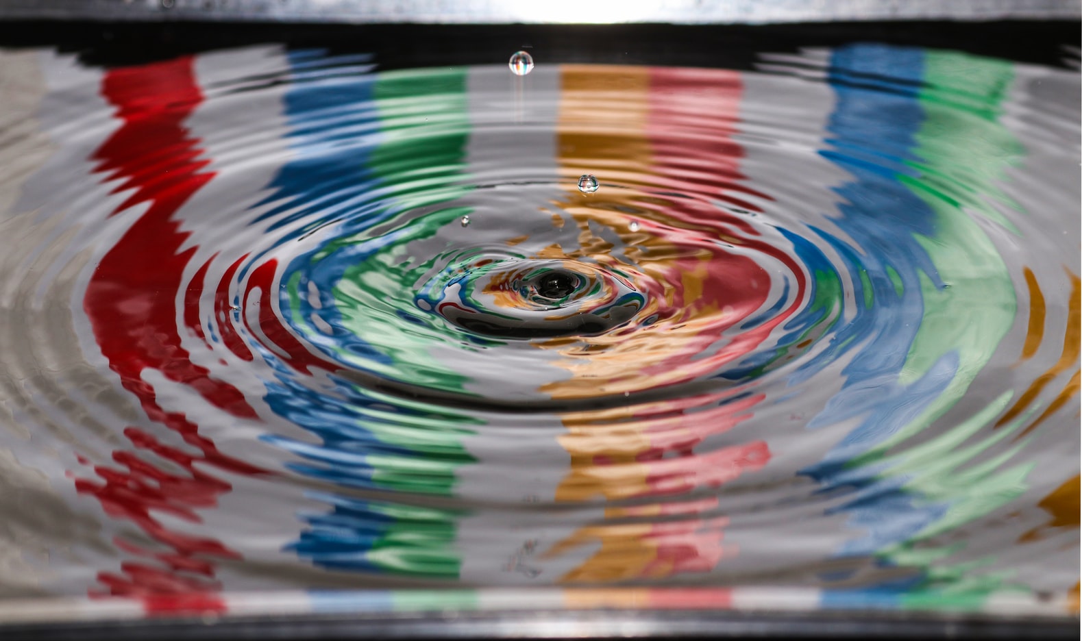 Colorful water ripples and droplets in reflective surface.