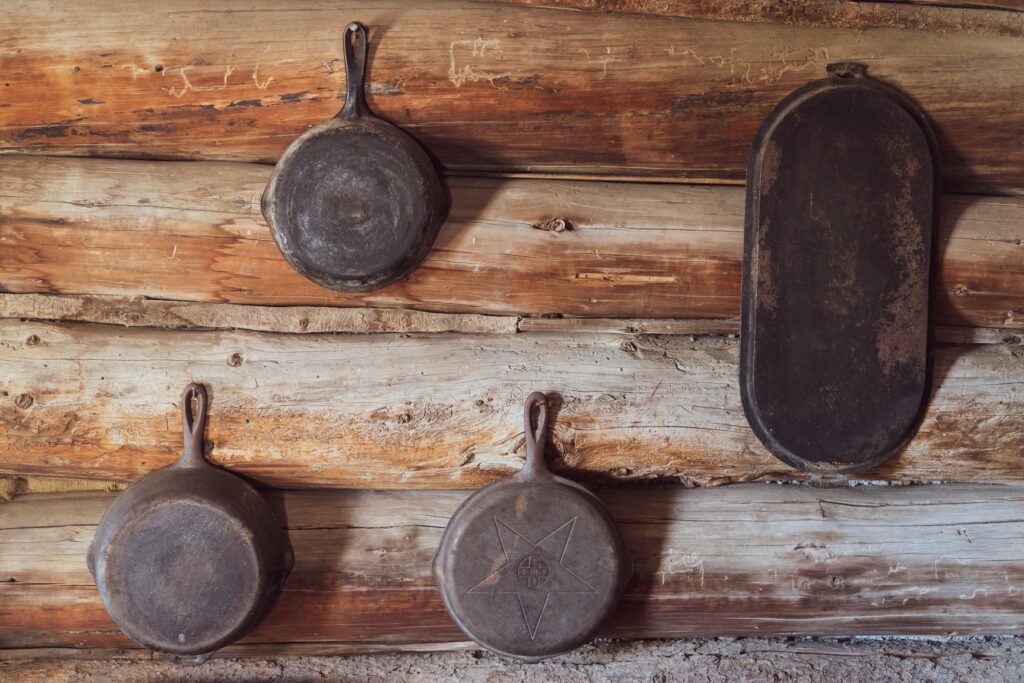 Vintage cast iron cookware on rustic wooden wall.