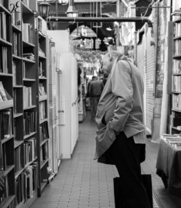 Elderly man browsing books in a busy market alley.