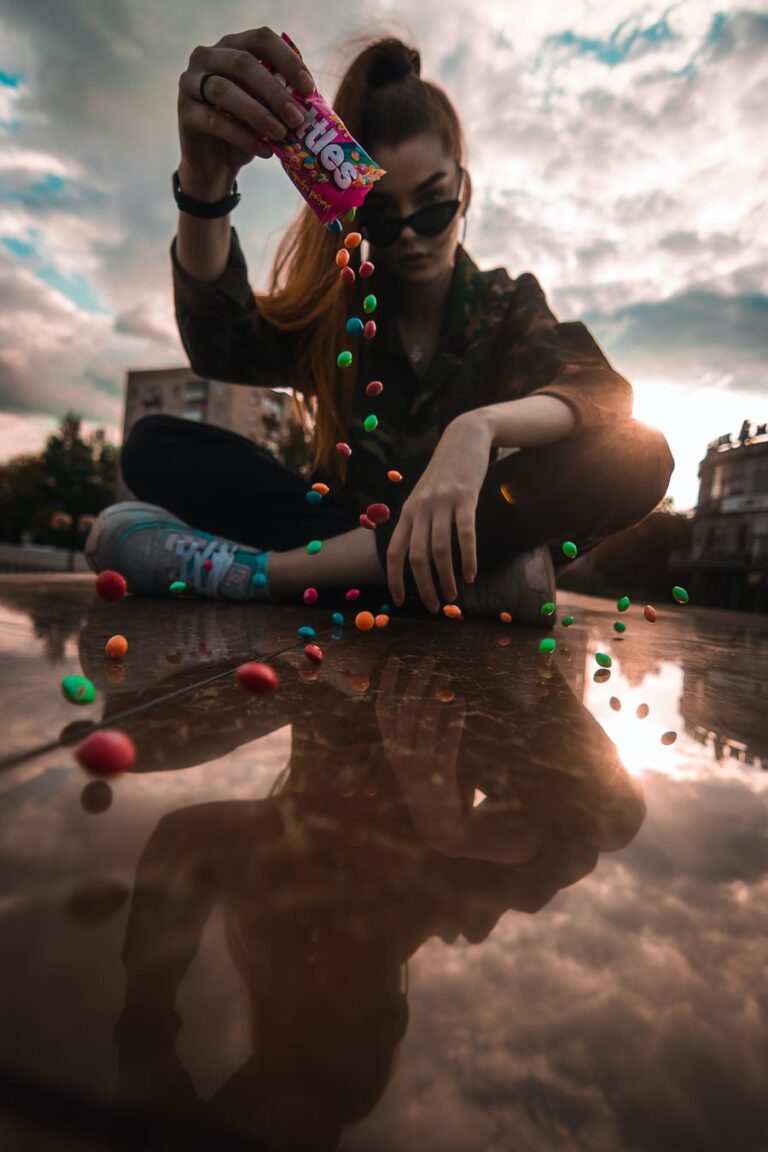 Woman pouring candies onto reflective surface at sunset.