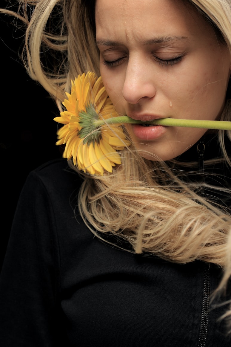 Woman holding sunflower with mouth, tear on cheek.