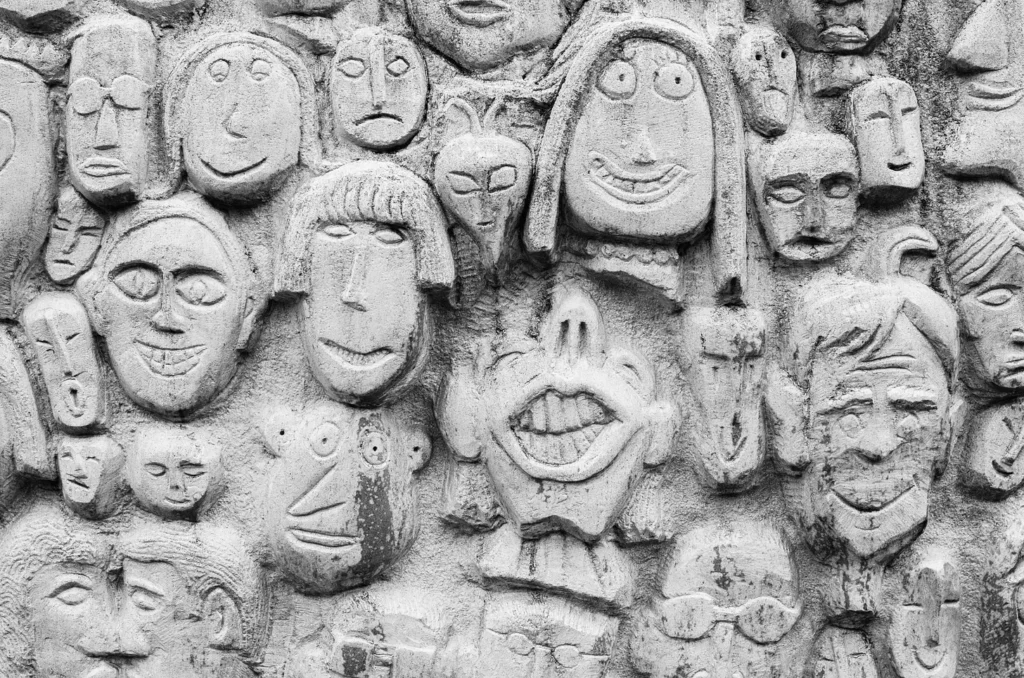 Textured wall with diverse bas-relief faces in grayscale.