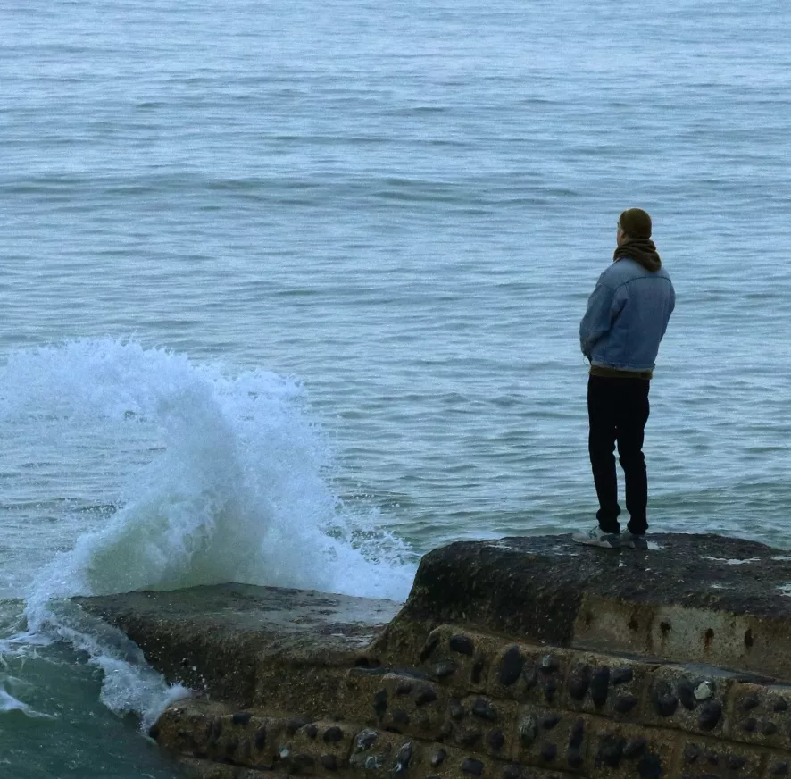 Person watching waves crash on rocky ledge by sea