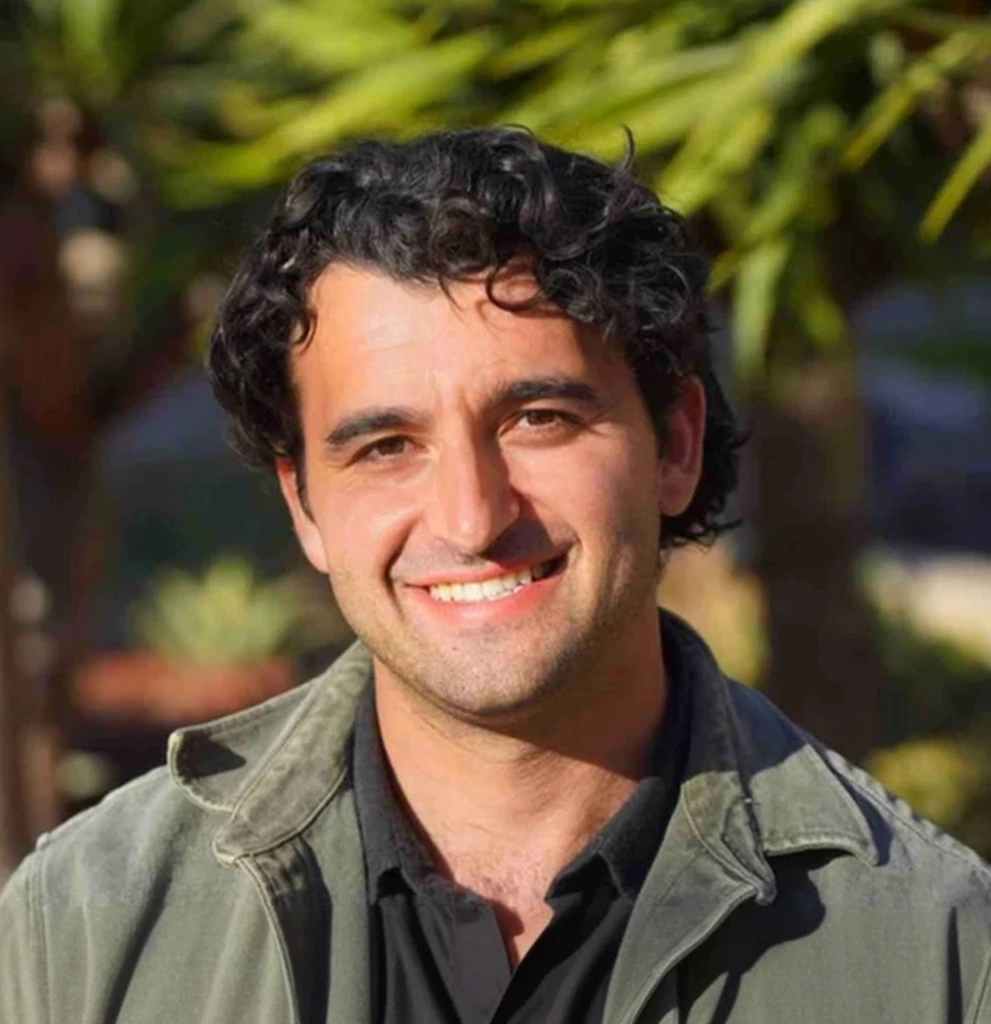 Smiling man outdoors with green plants in background