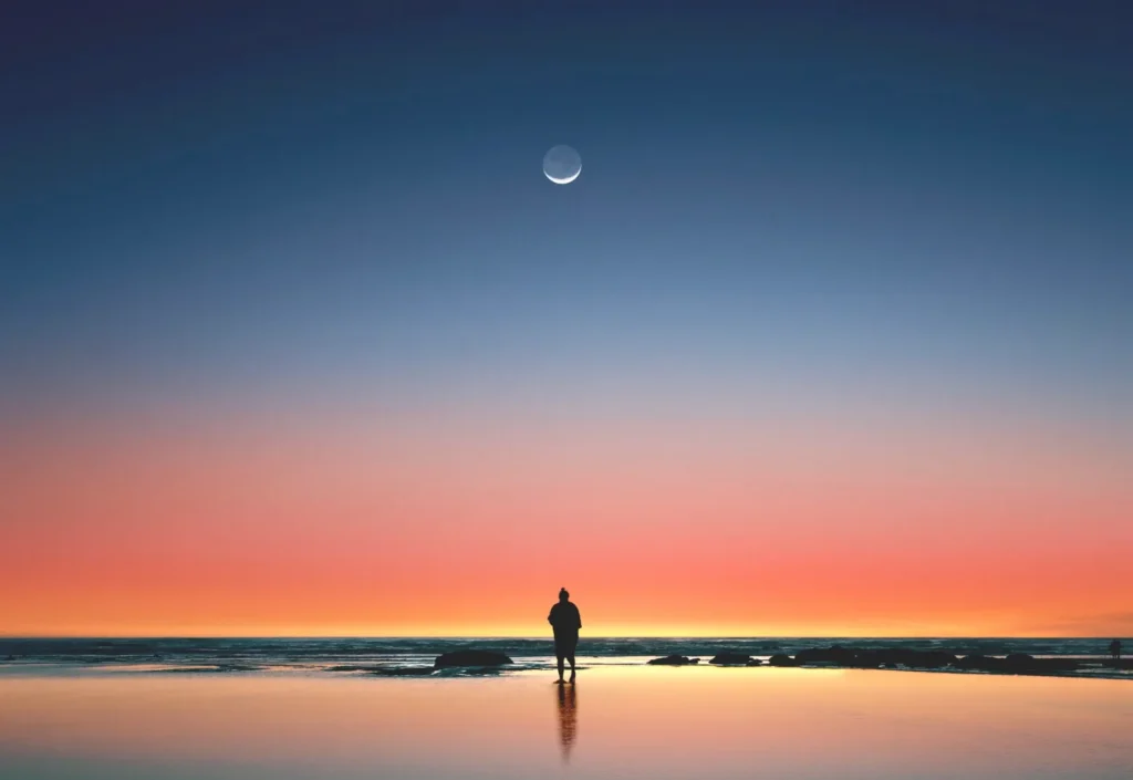 Person standing at beach under moon at twilight