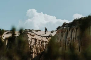 Person walking on sandy cliff under large clouds