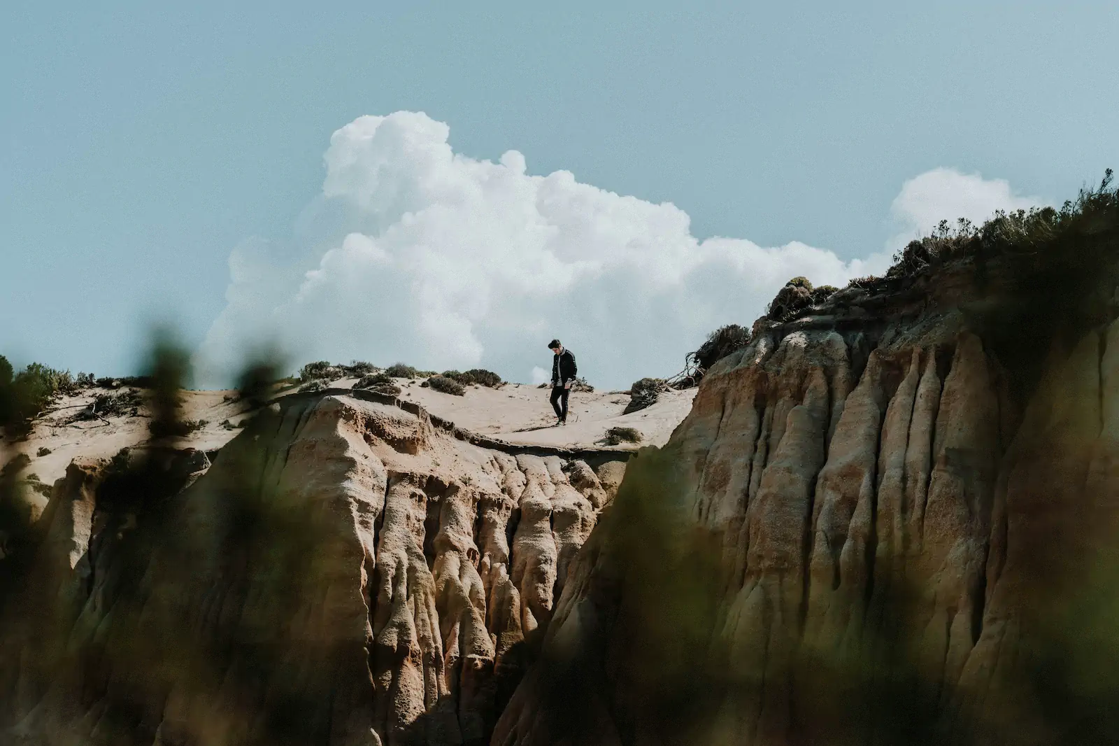 Person walking on sandy cliff under large clouds
